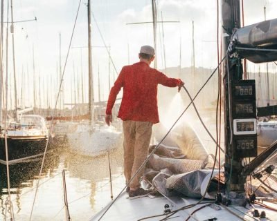 Limpieza-barcos-en-Barcelona hombre limpieando con una manguera la cubierta de un velero